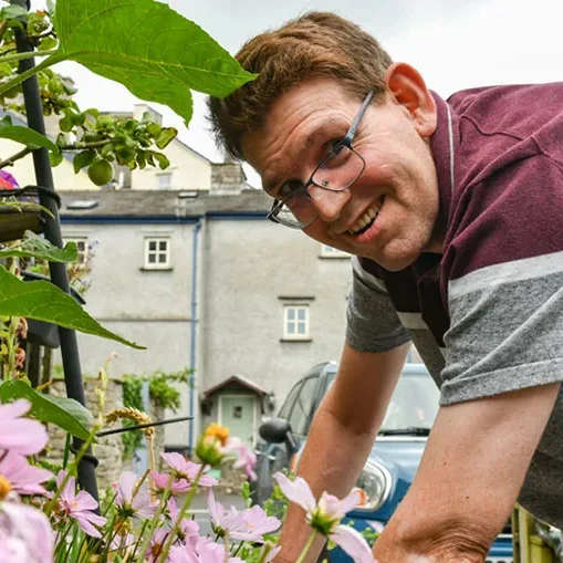 A happy man with a learning disability enjoying gardening outside his home