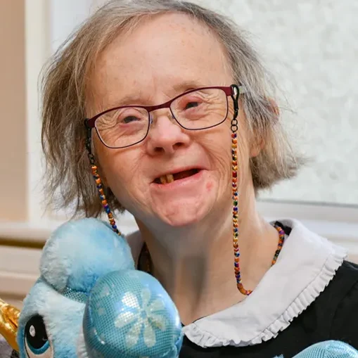A happy elderly lady with a learning disability cuddling a toy unicorn in her supported home