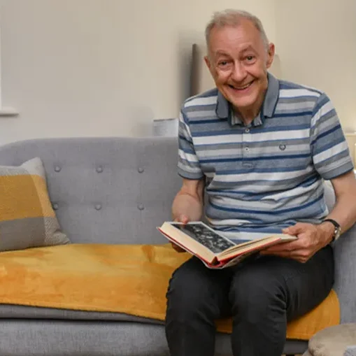 A happy gentleman with a learning disability enjoying looking at book whilst sat on a sofa in his home