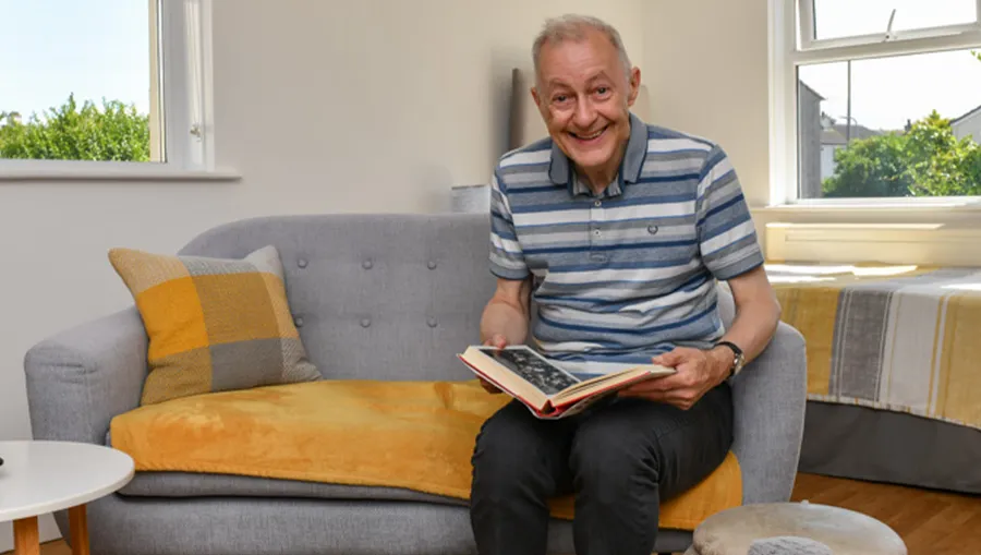 A happy gentleman with a learning disability enjoying looking at book whilst sat on a sofa in his home