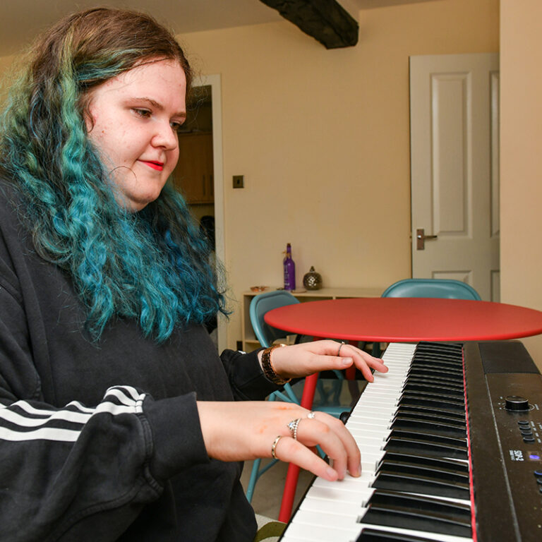 A tenant of Fairoak Housing Association playing piano in her home in Kendal